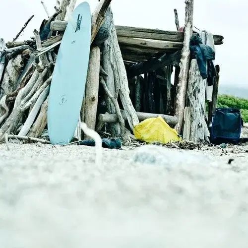 Reference photo of a driftwood beach shack with a pale blue surfboard leaning against it